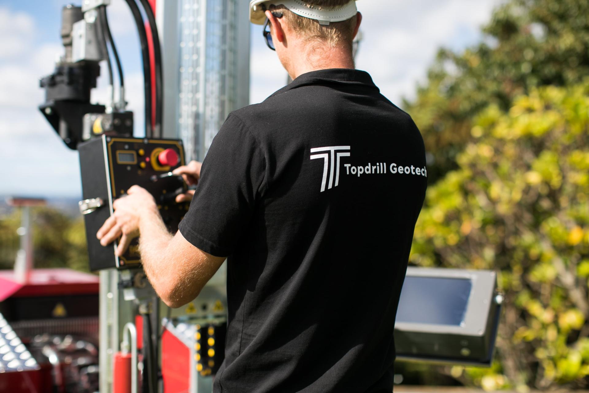 Back shot of man operating CPT machine, showing logo on t-shirt