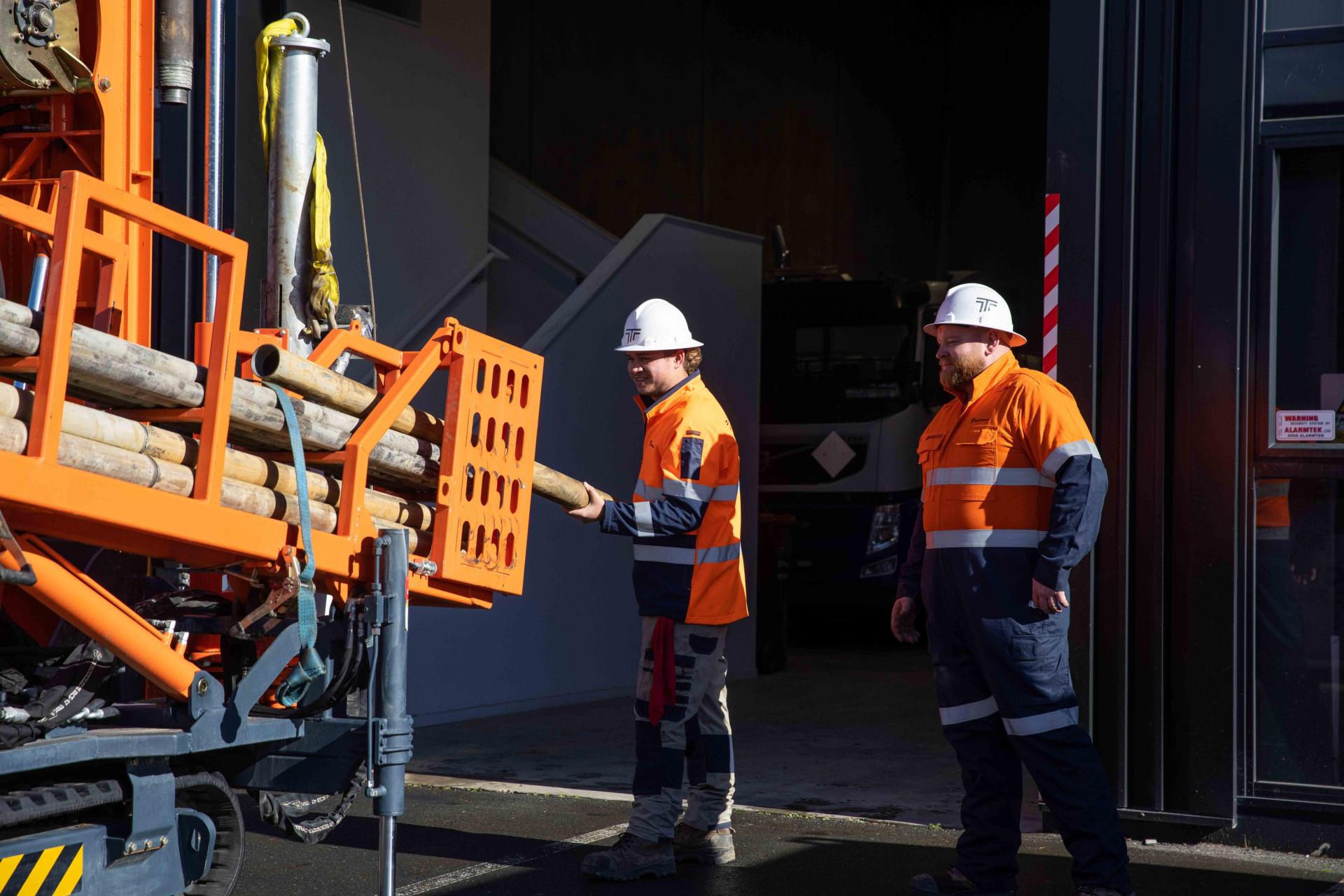 Two men loading materials onto borehole drilling machine. 